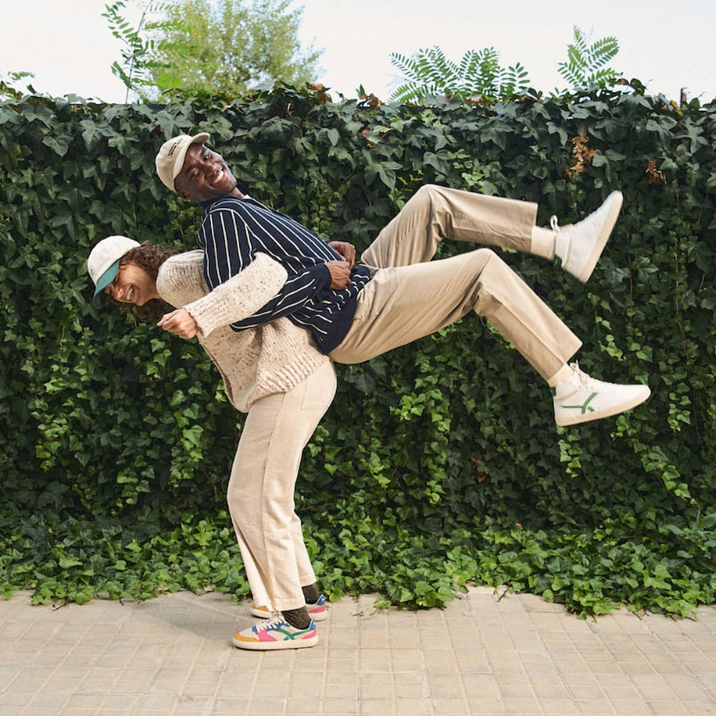 Two people in a playful pose against a green hedge.
