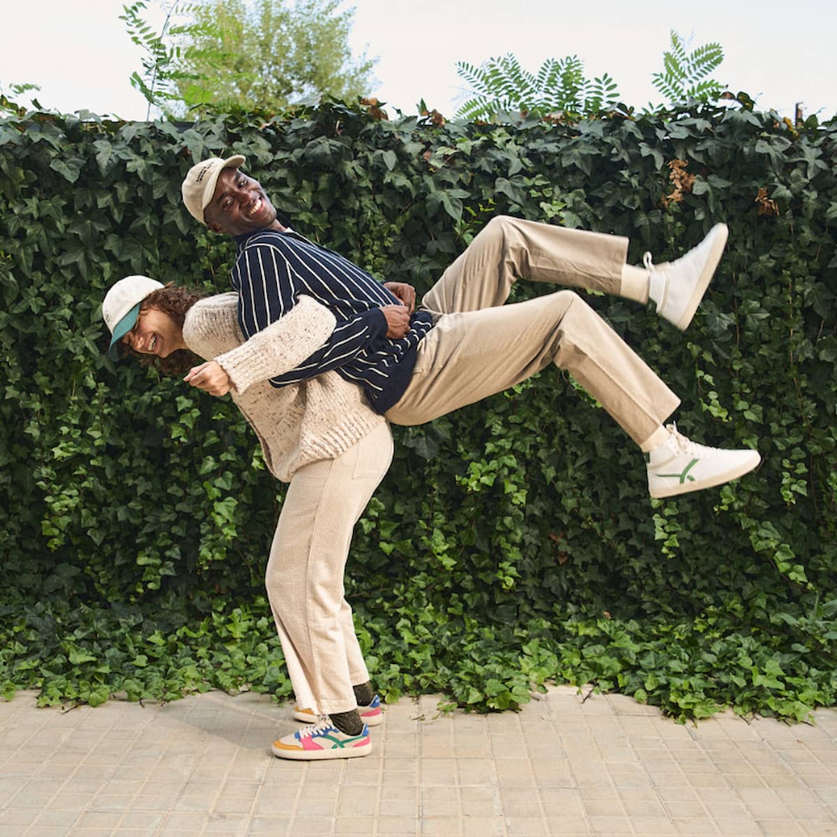 Two people in a playful pose against a green hedge.