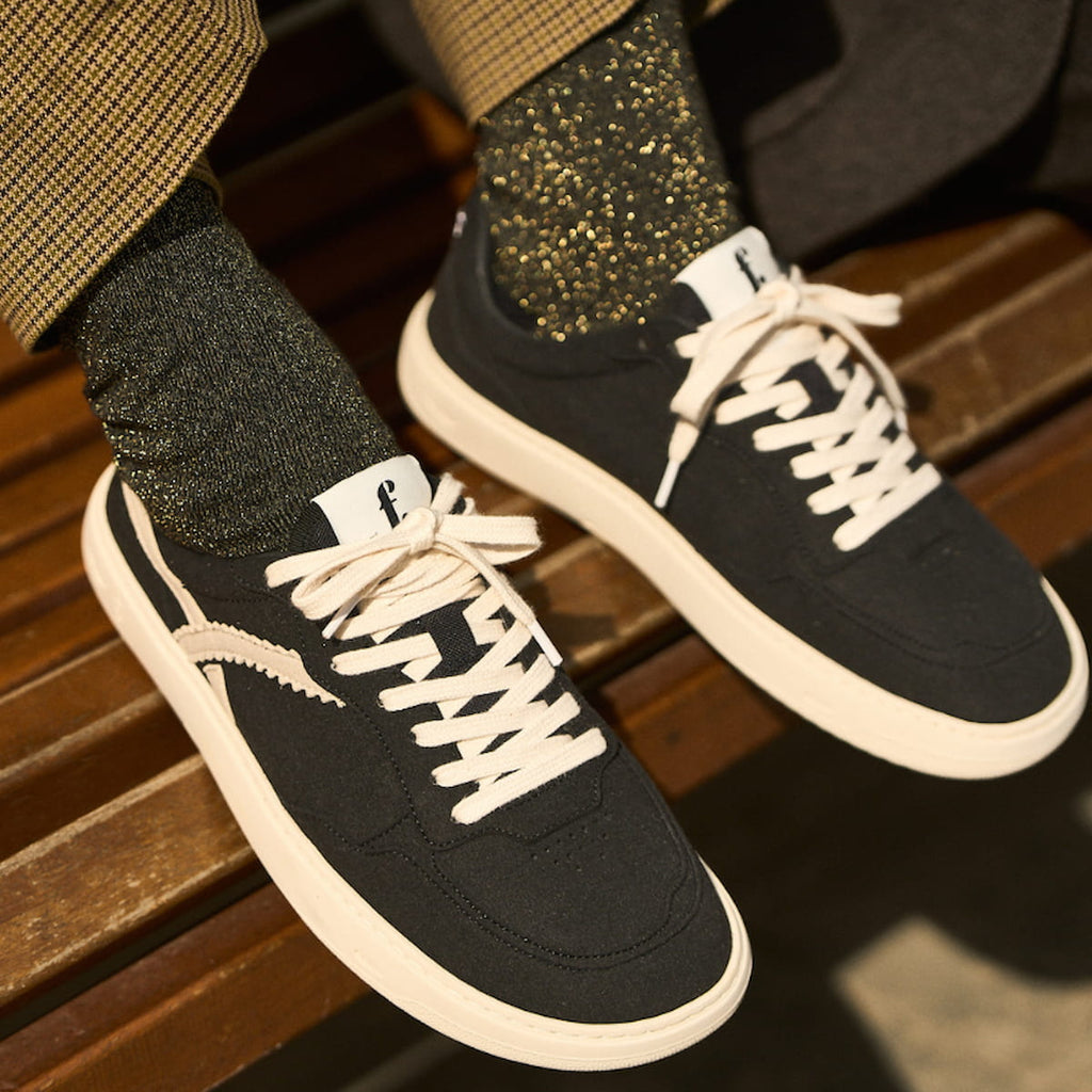Black minimalist sneakers with white soles worn on a wooden bench