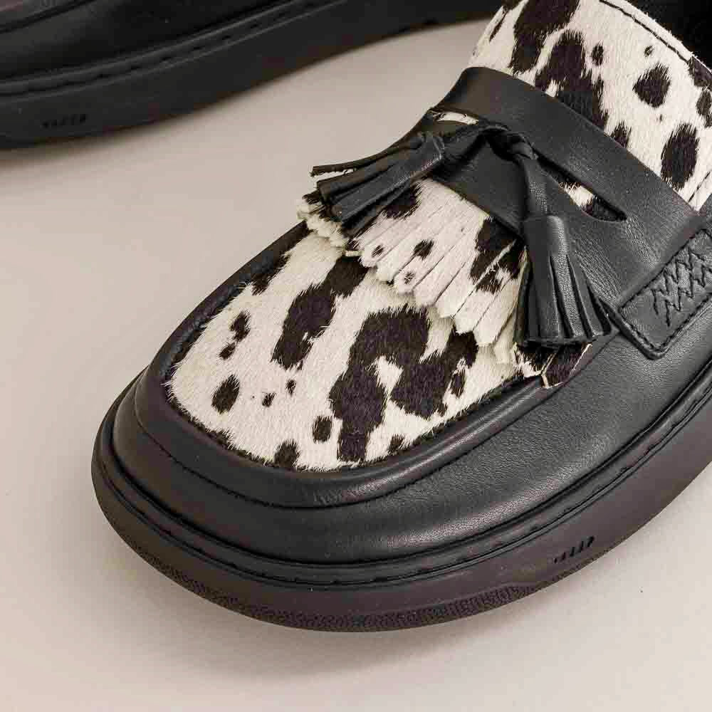 Black and white cow print loafer with tassel on a light gray background