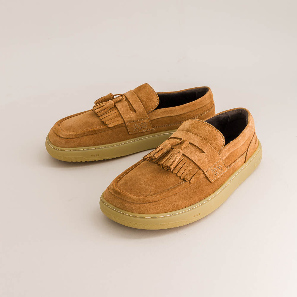Pair of tan suede barefoot loafers with tassels on a light beige background