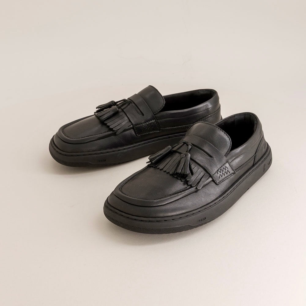 Pair of black barefoot loafers with tassels on a beige background