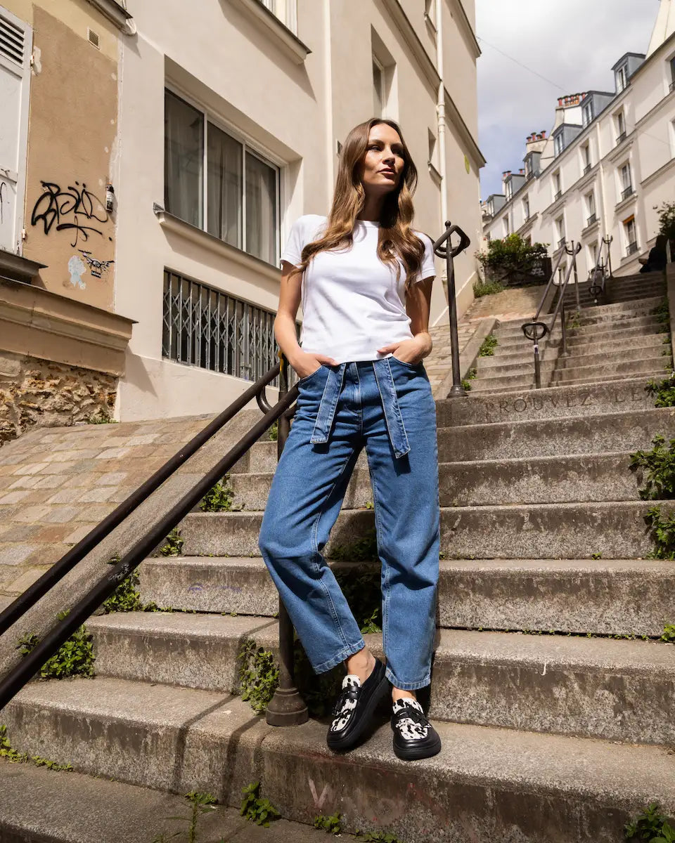 Woman in white shirt and blue jeans standing on stone steps in an urban setting