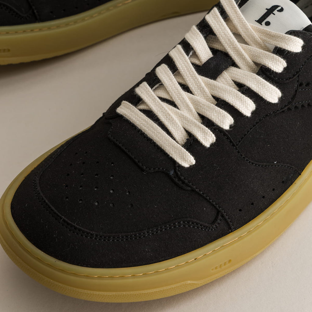 Black barefoot sneaker with white laces and yellow sole on a light background
