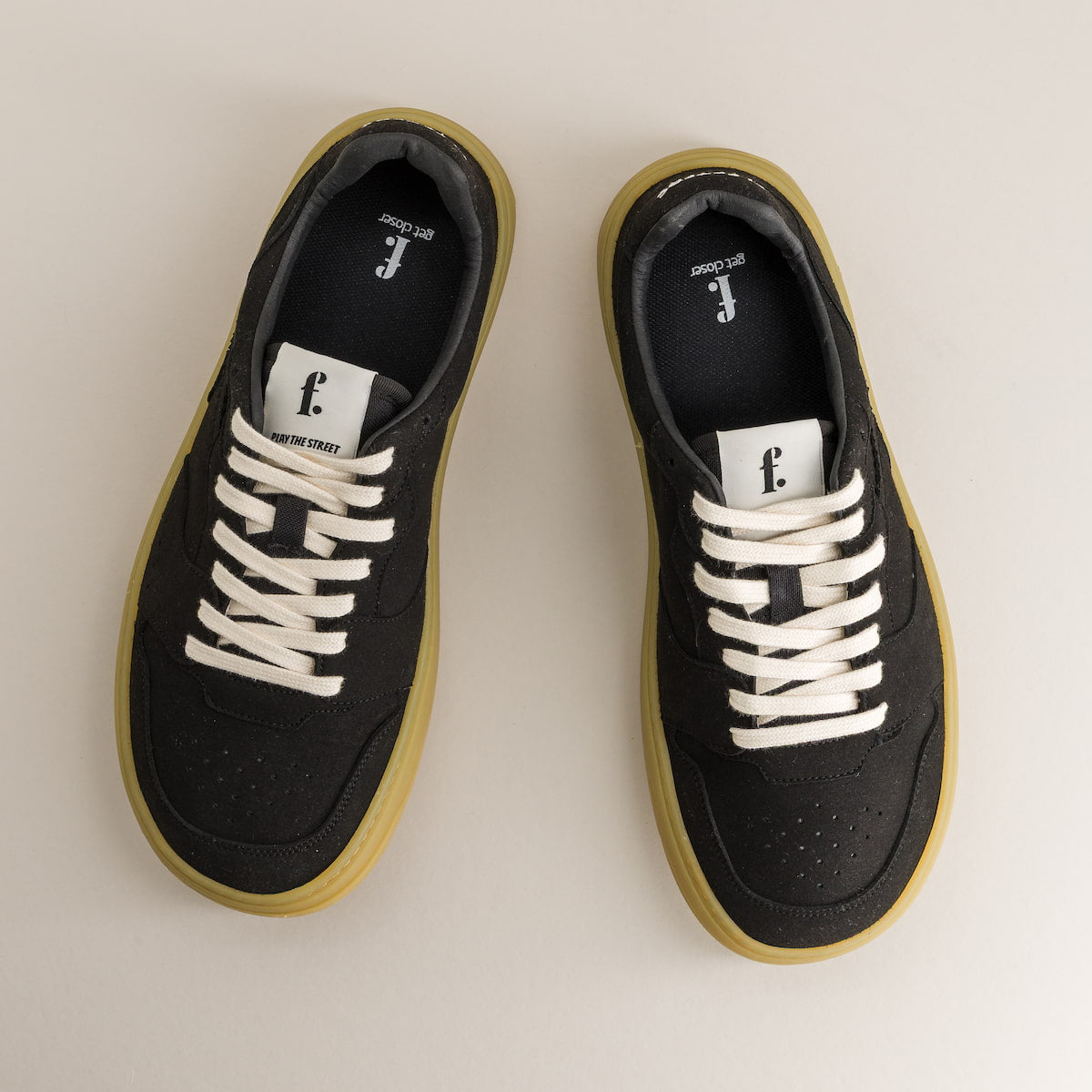 Black barefoot sneakers with white laces on a beige background