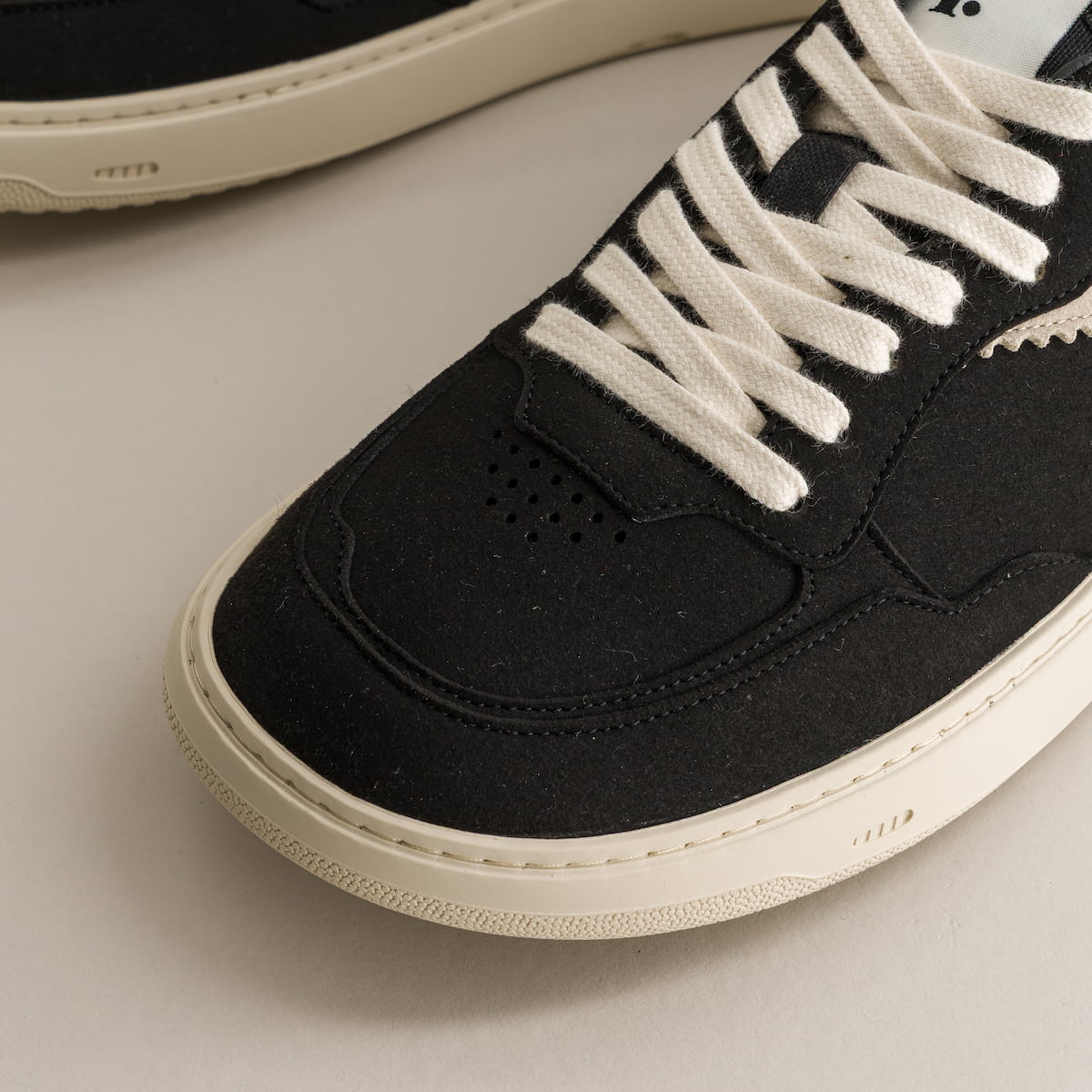 Black sneaker with white laces on a light gray background
