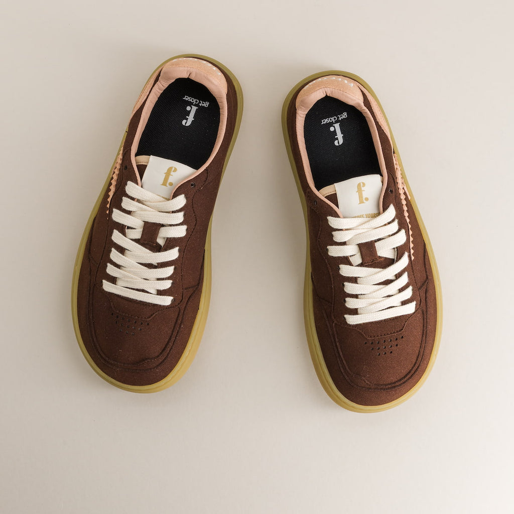 Pair of brown sneakers with white laces on a light beige background
