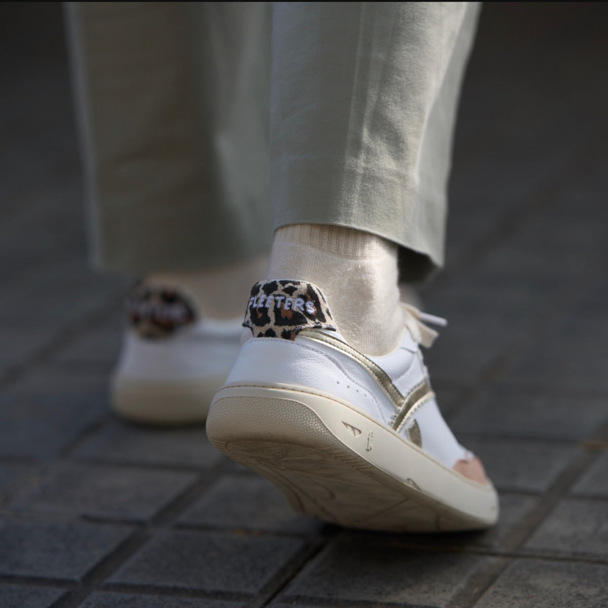 A person wearing white, pink, gold, and leopard-print barefoot sneakers.
