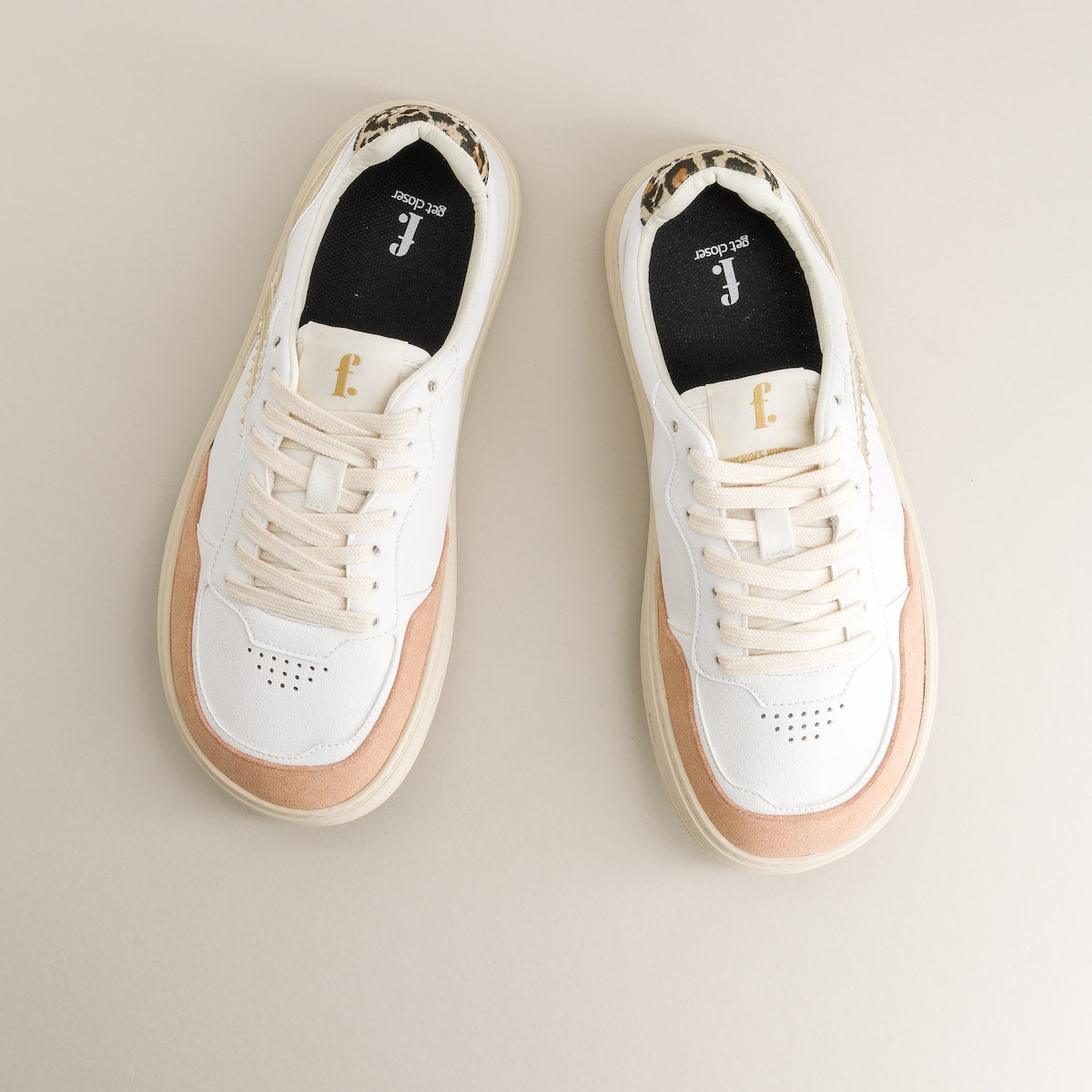 Pair of white minimalist sneakers with tan soles on a beige background