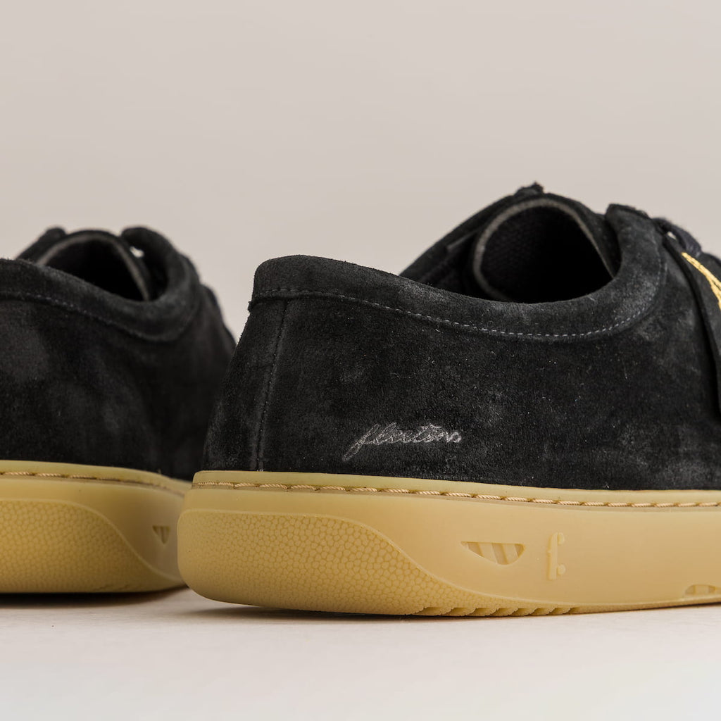 Black suede sneakers with tan soles on a neutral background