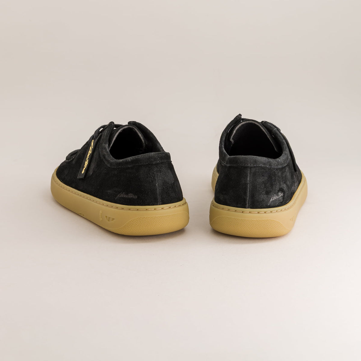 Pair of black sneakers with tan soles on a light beige background