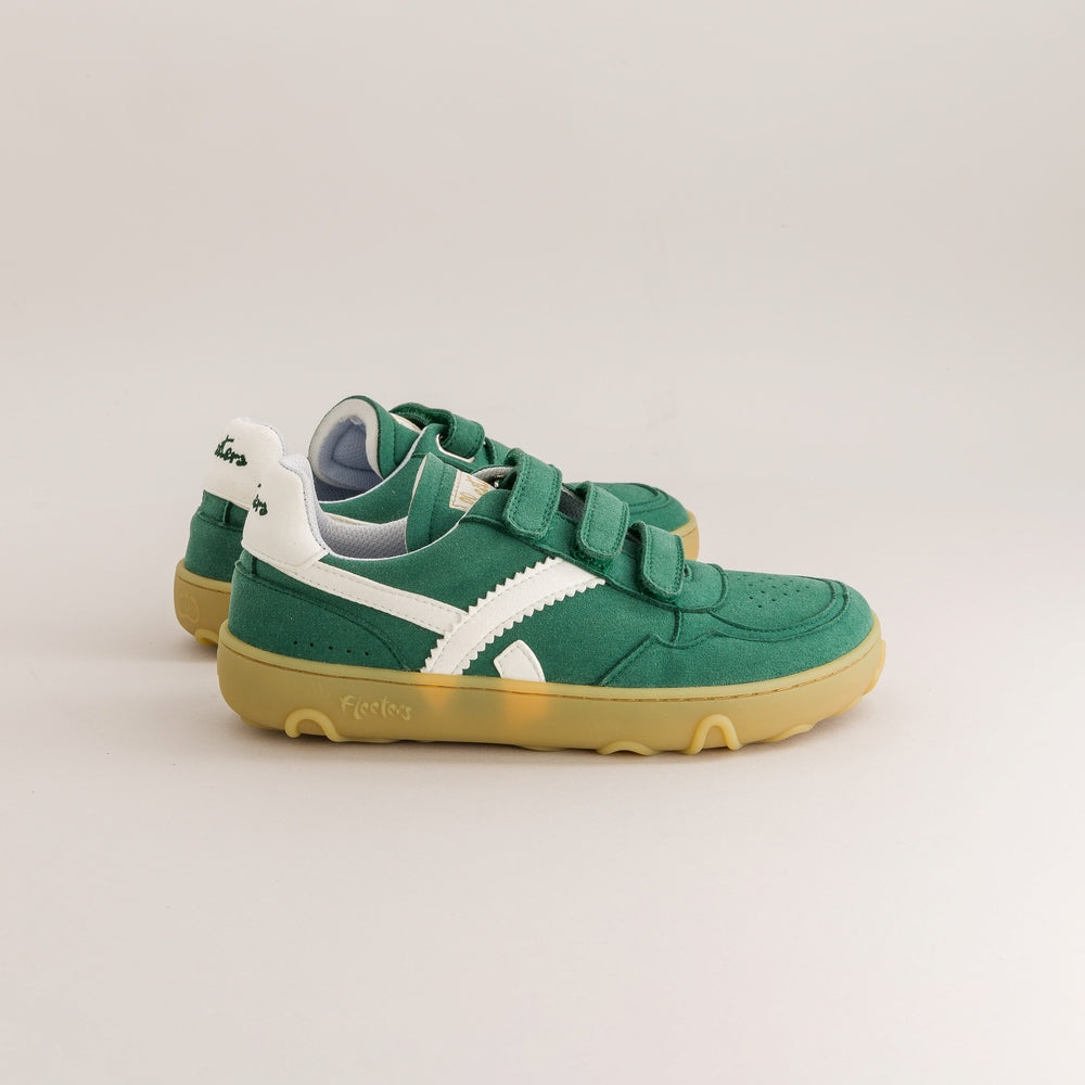 Une paire de baskets barefoot pour tout-petit, vertes avec bandes latérales blanches, double bande auto-agrippante et semelles gomme, photographiées sur fond gris studio.