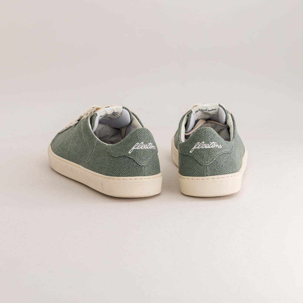 A pair of green wool low-top sneakers shown from the back, featuring white soles and the brand name 'fleeters' embroidered on the heel, set against a plain light beige background.