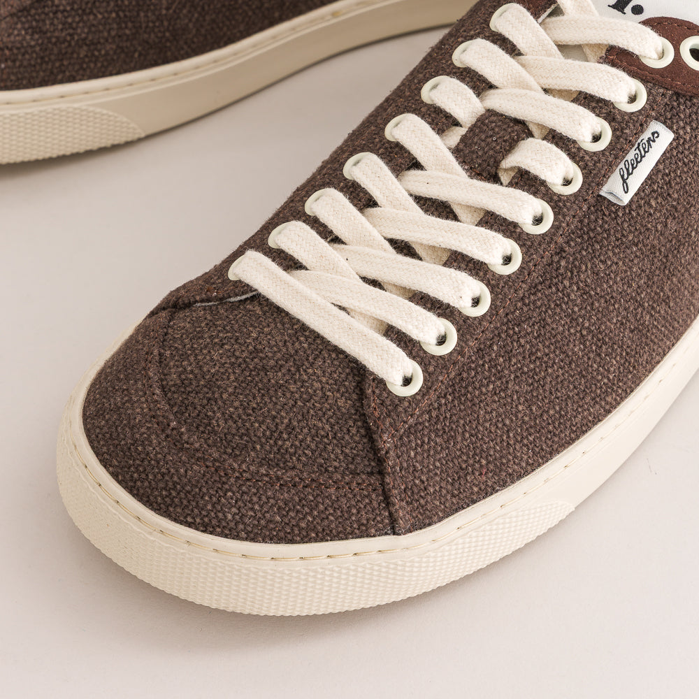 A close-up of a brown wool low-top sneaker with white laces and a cream-colored rubber sole, featuring a small white 'Fleeters' brand tag on the side.