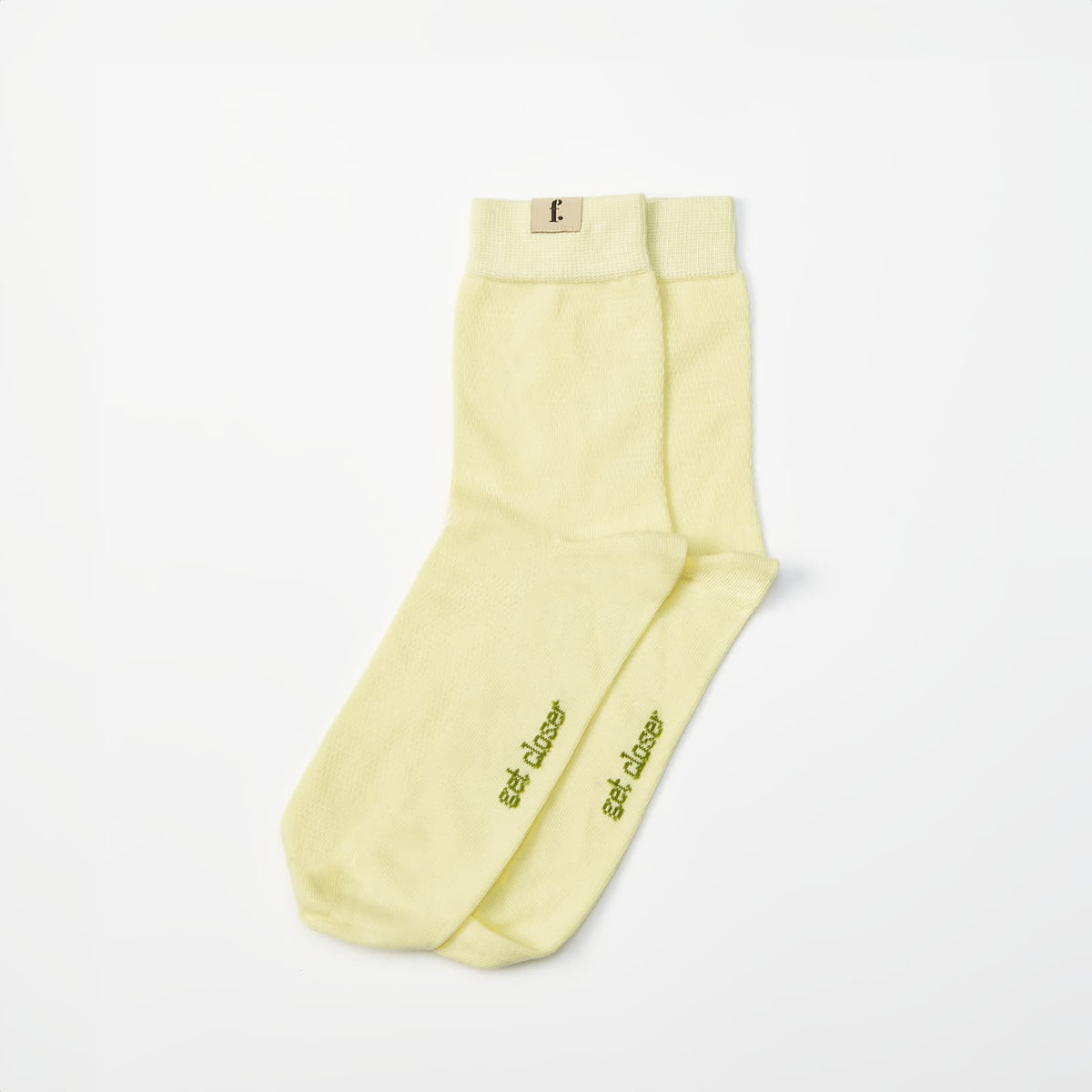 A pair of pale yellow barefoot socks with olive green embroidered text reading 'get closer' on the toes, displayed on a clean white background.