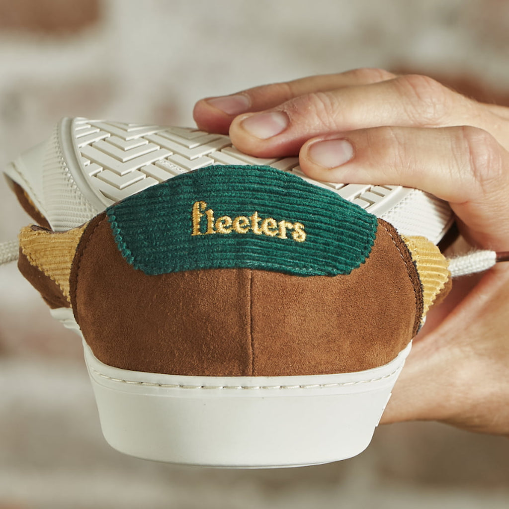 Close-up of a barefoot shoe with 'fleeters' branding held by a hand against a neutral background