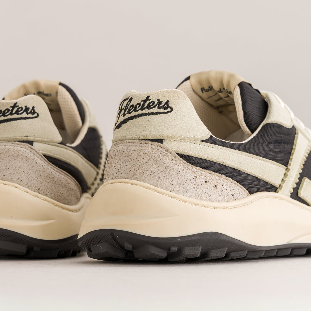 Close-up of a pair of low-top minimalist sneakers showing the heel and side panels, featuring cream, beige, and black colors with 'Fleeters' branding on the heel tab.