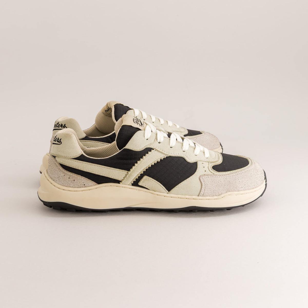 A pair of vintage-style platform barefoot sneakers in cream, black, and light gray suede, shown from a side profile against a neutral light gray background.
