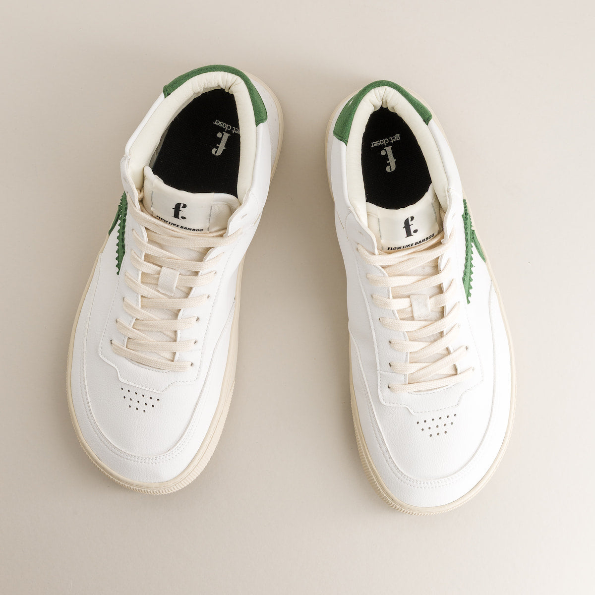 Pair of white barefoot sneakers with green accents on a beige background