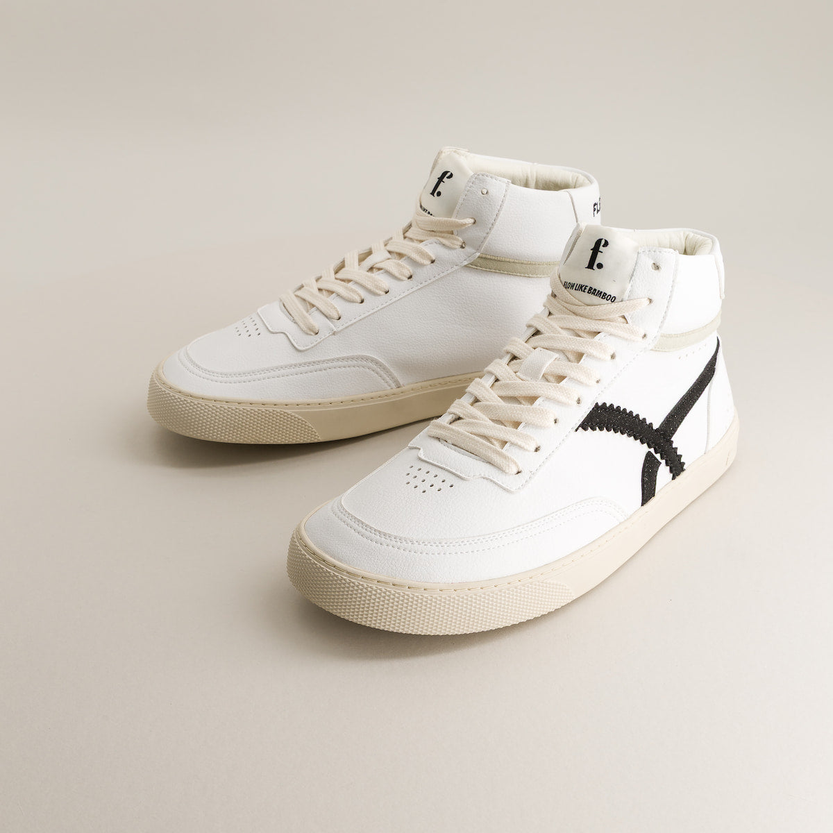 White high-top barefoot sneakers with a black logo on a beige background