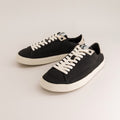 A pair of black canvas low-top barefoot sneakers with off-white laces and off-white rubber soles, displayed on a clean light gray studio background.