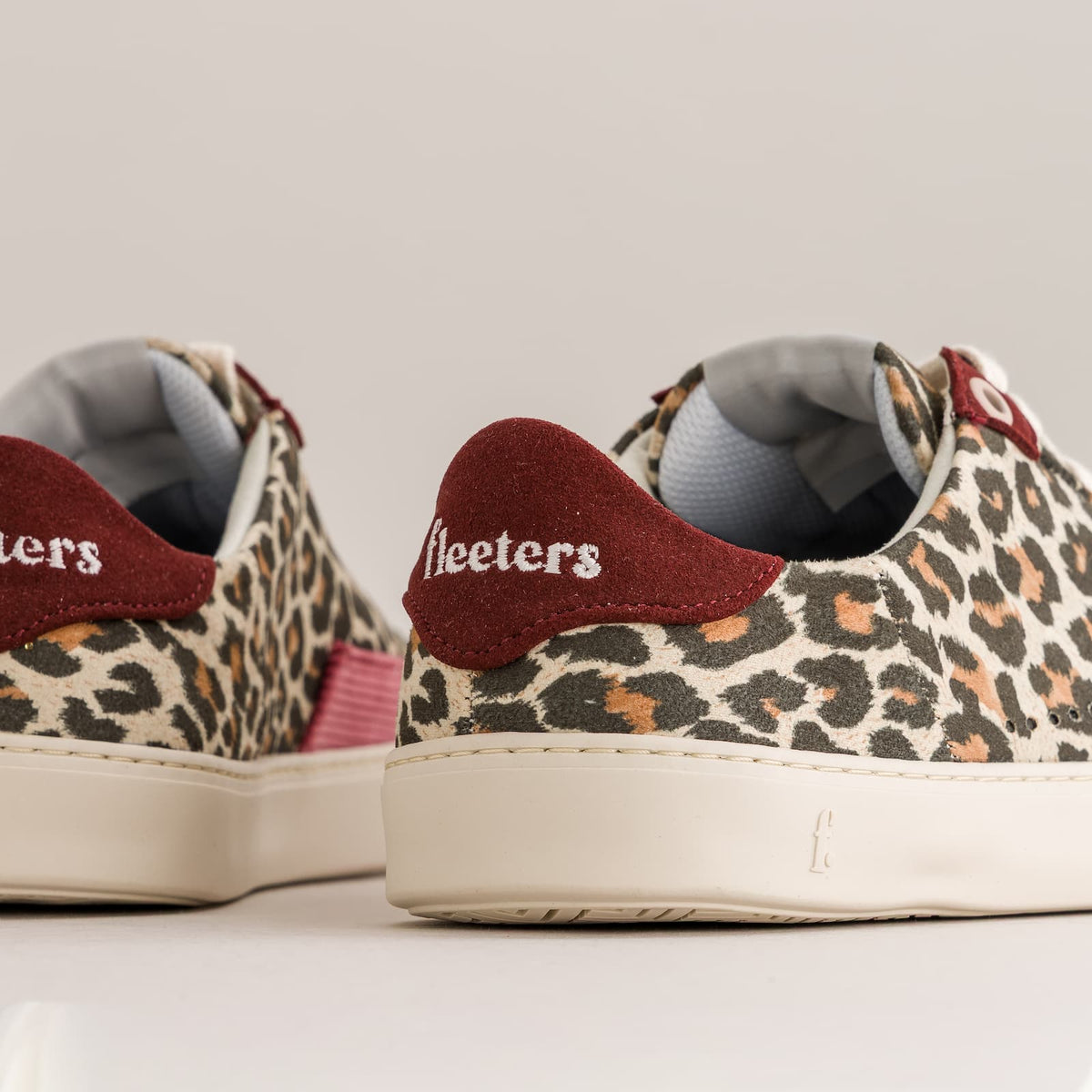 A pair of low-top barefoot sneakers with a leopard print canvas upper, cream rubber soles, and burgundy heel tabs with white 'fleeters' branding, shown on a light gray background.