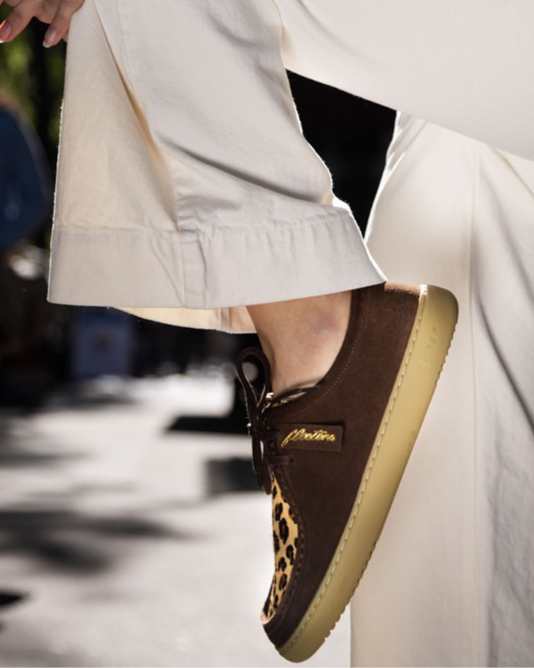 Brown barefoot derby with a leopard print sole worn by a person in white pants.